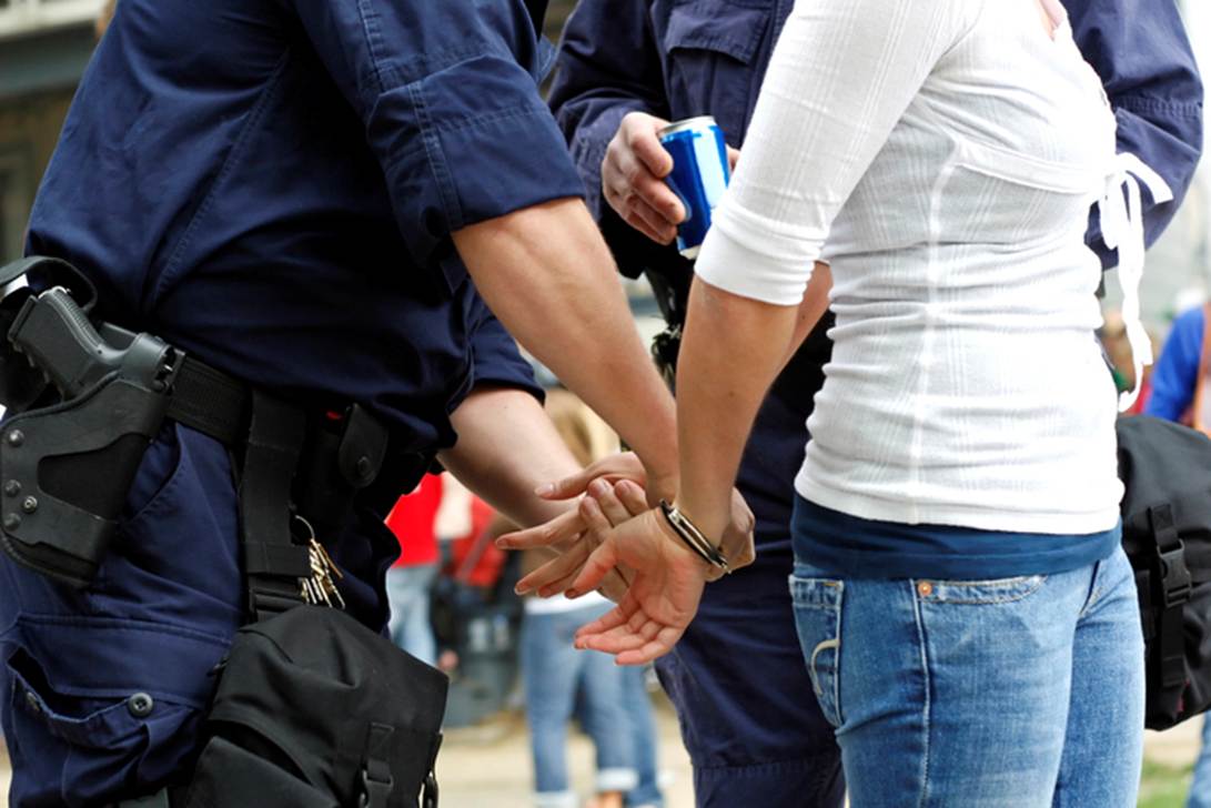 Two uniformed police officers arrest a woman, handcuffing her. This image illustrates key landmark police brutality cases in New York, as highlighted in the article.